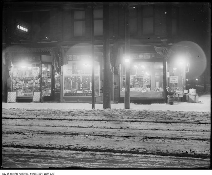 Exterior view of store fronts at 1498 Queen Street West, Parkdale, with Humphrey gas arc lighting: Sutherland tobacco, A. Grapple shoes, F. G. Martin, grocer. - [ca. 1922]