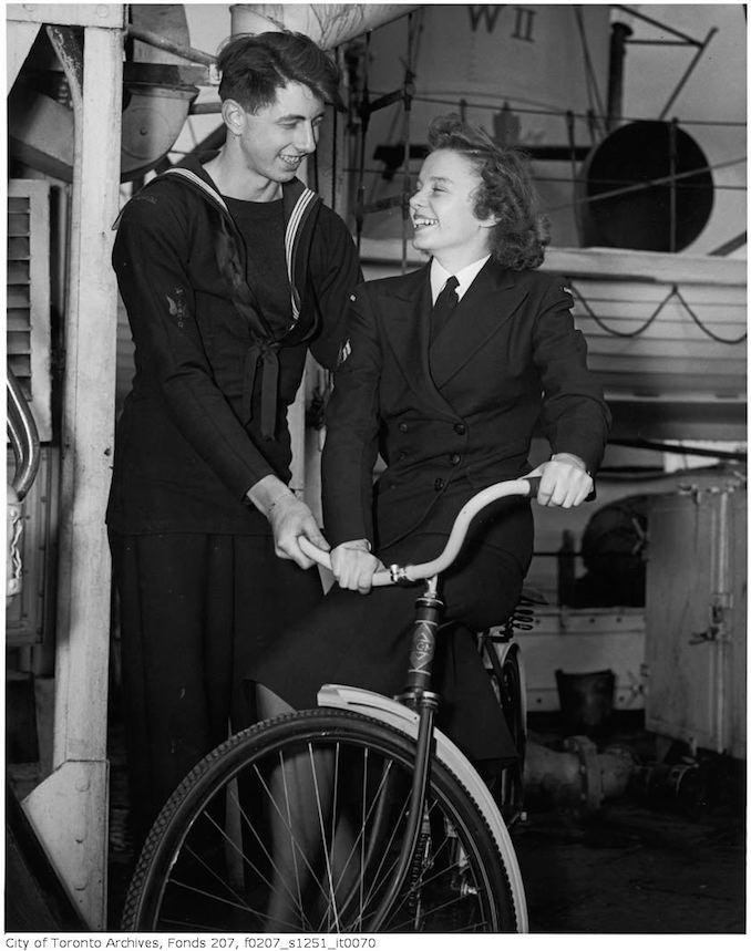 Mary J. Gilmore and Ordinary Seaman Robert Denyer try out one of the bicycles - HMCS "Forest Hill" crew host WRENS stationed in Halifax from Forest Hill Village, and other parts of Toronto at a dinner on the ship : Coder James Cramer (1300 Lansdowne Ave.) shows WREN Ruth Arnsby (9 Montclair) one of the bicycles sent by the Village of Forest Hill to the ship 1940-45 - Vintage Bicycle Photographs