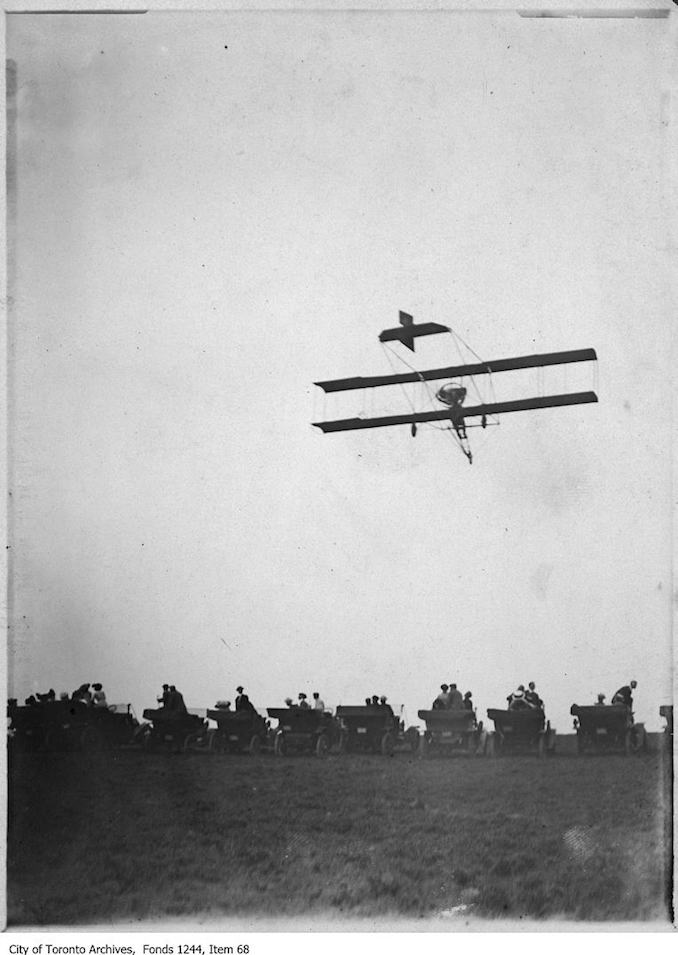 photograph of an airplane in flight. Information provided by a researcher indicates that the airplane is probably a Curtiss-type Pusher bi-plane with inset ailerons and rotary engine, flown by Charles F. Willard, and that the event may be the Aviation Meet held at Donlands Farm, Todmorden Mills, August 3-5, 1911.