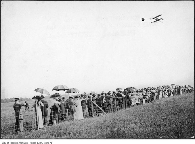 photograph of an airplane in flight over a crowd. Information provided by a researcher indicates that the airplane is probably a Curtiss-type Pusher bi-plane with inset ailerons and rotary engine, flown by Charles F. Willard, and that the event is probably the Aviation Meet held at Donlands Farm, Todmorden Mills, August 3-5, 1911.