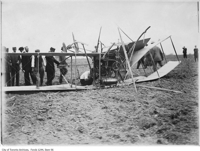 Men inspecting wreckage of first Toronto airplane crash. - 1911 - photograph of an airplane crashed on the ground. Information provided by a researcher indicates that it is probably a bi-plane with 7-cylinder Gnome rotary engine, flown by J.A.D. McCurdy, and that the event is probably the Aviation Meet, Donlands Farm, Todmorden Mills, August 3-5, 1911.