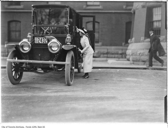 Miss Dyment talking to driver of automobile at auto show, Armouries 1912