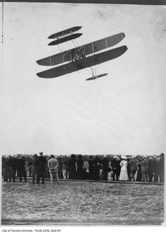 Ralph Johnstone flying box kite airplane. - July, 1910 - photograph of an airplane in flight. Information provided by a researcher indicates that the airplane is probably a 1909 Model A (Transitional) bi-plane flown by Ralph Johnstone of the Wright Exhibition Company, and that the event is probably the Ontario Motor League Aviation Meet held at Trethewey Model Farm, Weston, July 8-16, 1910.