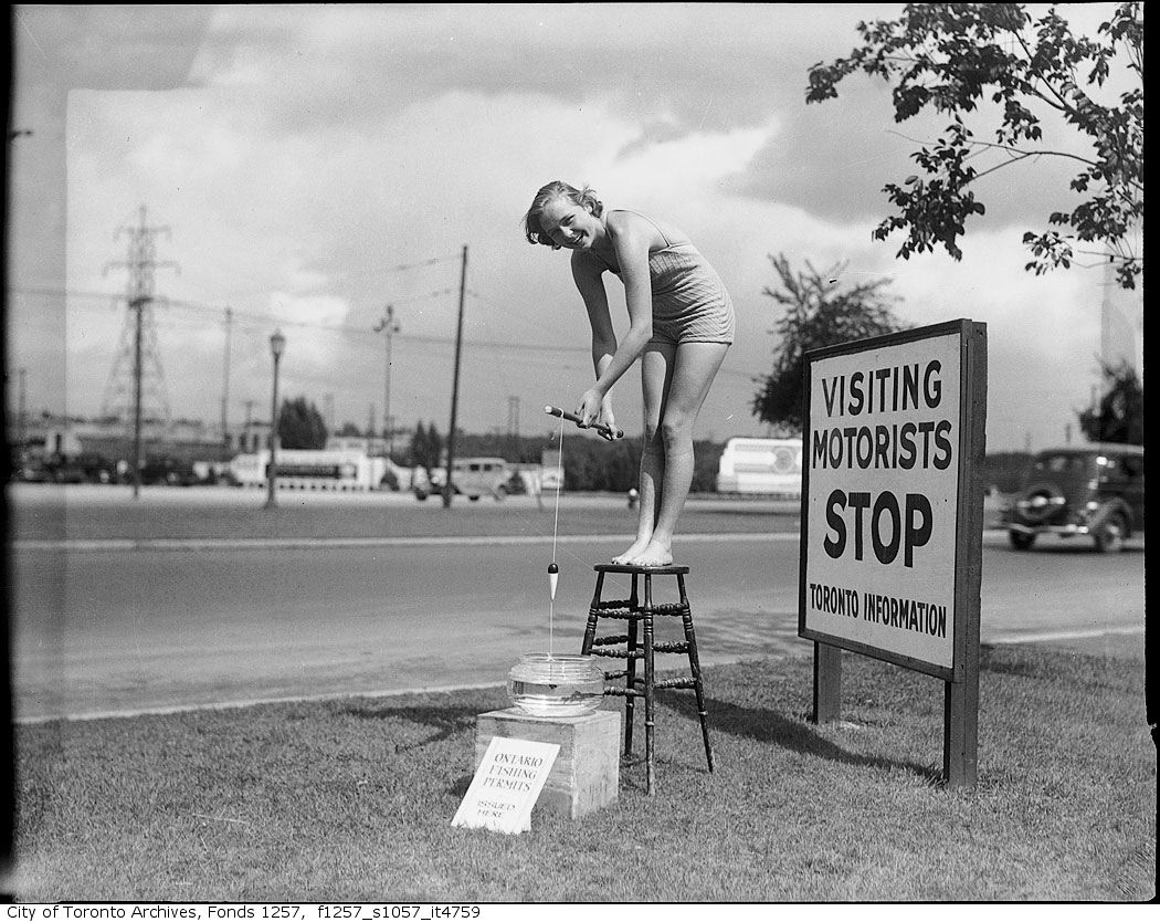 193? - Woman fishing in gold fish bowl outside Toronto information booth - Vintage Fishing Photographs