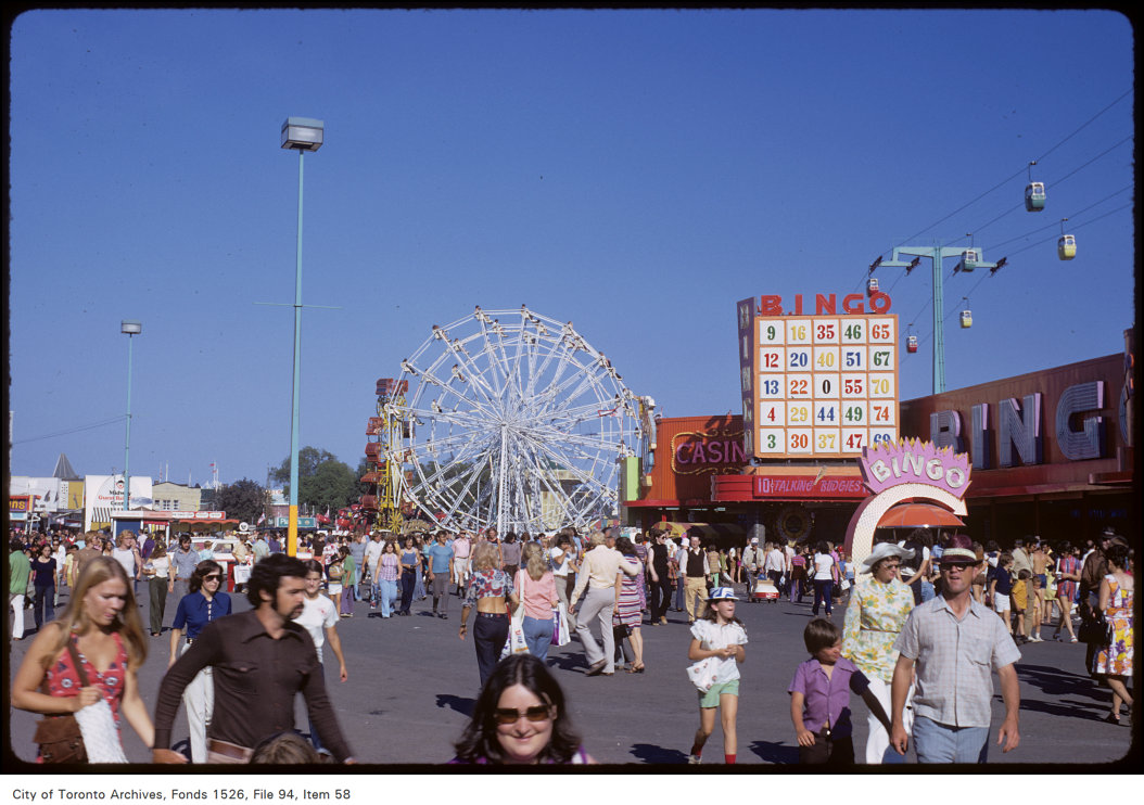 1972 - View of crowds on CNE grounds, ferris wheel and bingo and casino buildings in the background