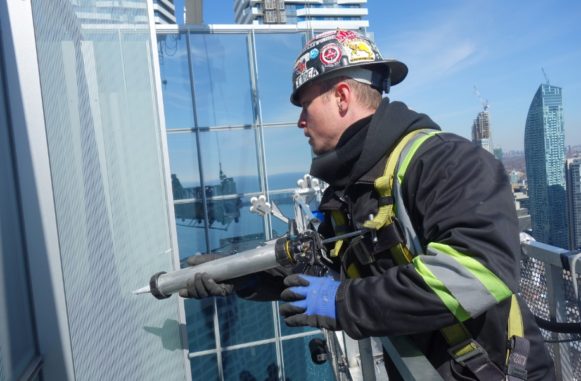 Chris caulking windows in a high rise office tower