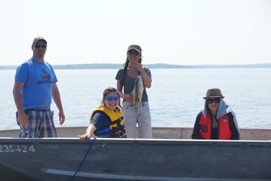 Fishing shot- Lora Kikuchi, in yellow life vest, looks on as one of the Teach for Canada teachers catches a fish during the community visit at Big Grassy River First Nation in late July.