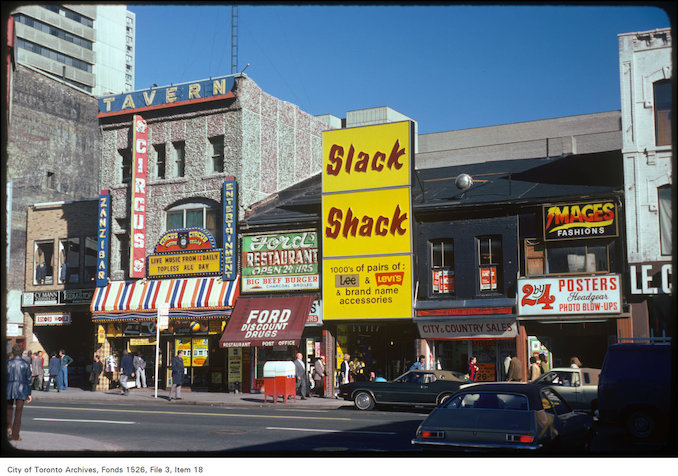 1975 - View of storefronts along Yonge Street on the east side, opposite Elm Street