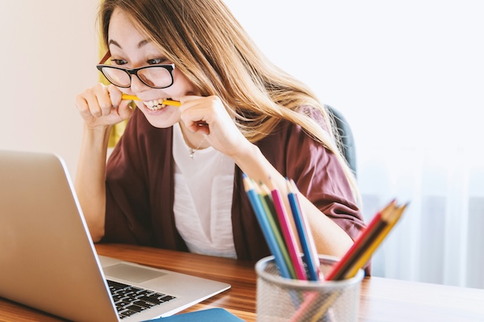 Woman on a laptop studying and biting a pencil.