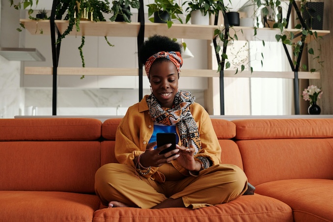 Photo of woman using a cell phone on her orange couch.ile-smiling-5711715/